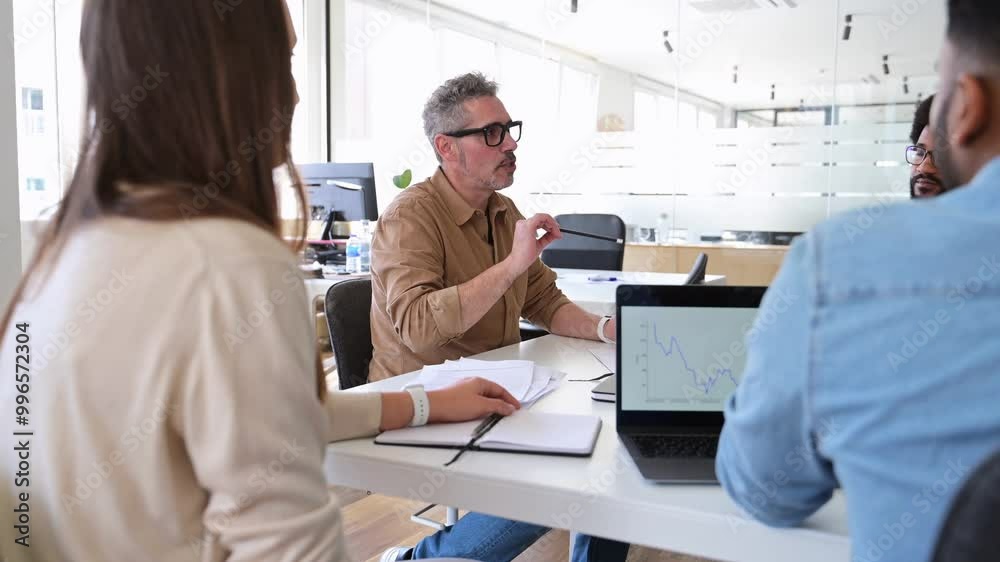 A mature professional man in a tan shirt talking with colleagues out of focus in the foreground, exemplifying a supportive and collaborative office environment during a productive meeting A mature professional man in a tan shirt talking with colleagues out of focus in the foreground, exemplifying a supportive and collaborative office environment during a productive meeting