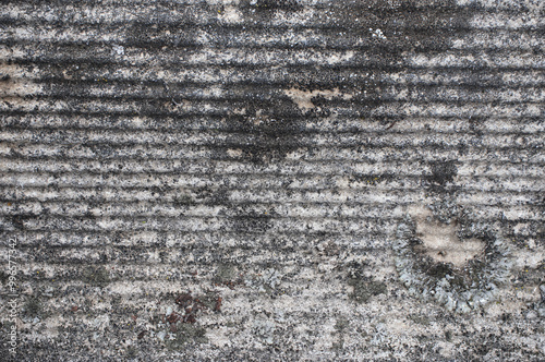 A close-up view of an old asbestos roof, showcasing its rough, weathered texture. The image highlights the aged material and worn details