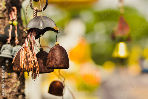 Rustic Wind Chimes Hanging from Tree, Close-Up of Weathered Bells with Vibrant Background, Stock Image for Meditation, Serenity Concepts, Spiritual Photography, and Peaceful Outdoor Settings.