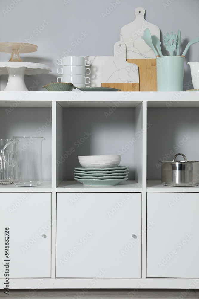 Shelving unit and storage cabinet with kitchenware near grey wall indoors Shelving unit and storage cabinet with kitchenware near grey wall indoors