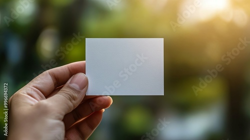 A Hand Holding a Blank White Card Against a Blurred Green and Yellow Background