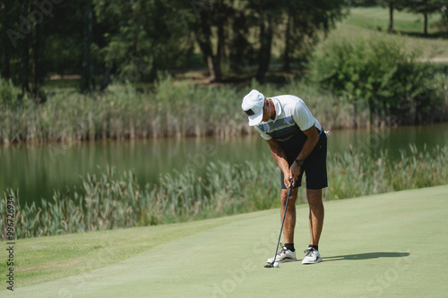 A golfer practices putting on a lush green course beside a tranquil lake on a sunny afternoon