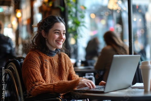 A woman in a wheelchair working on a laptop in a inclusive work environment, cafe, smiling as she watches a funny video with her friend, coworking modern lifestyle at remote job