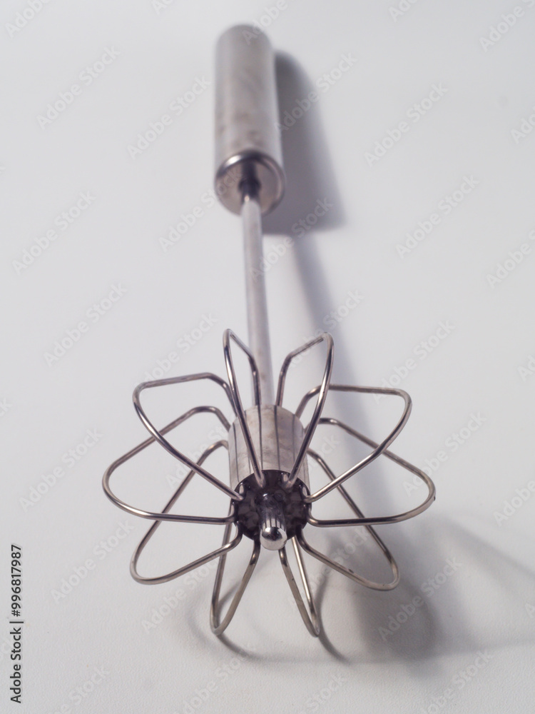 Manual mixer with spring, made of stainless steel on a white background, pressing the handle causes the tip of the tool to rotate as a mixer Manual mixer with spring, made of stainless steel on a white background, pressing the handle causes the tip of the tool to rotate as a mixer