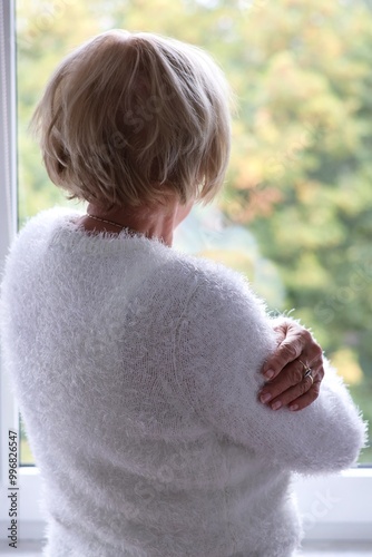 A lonely elderly woman standing at the window and waiting