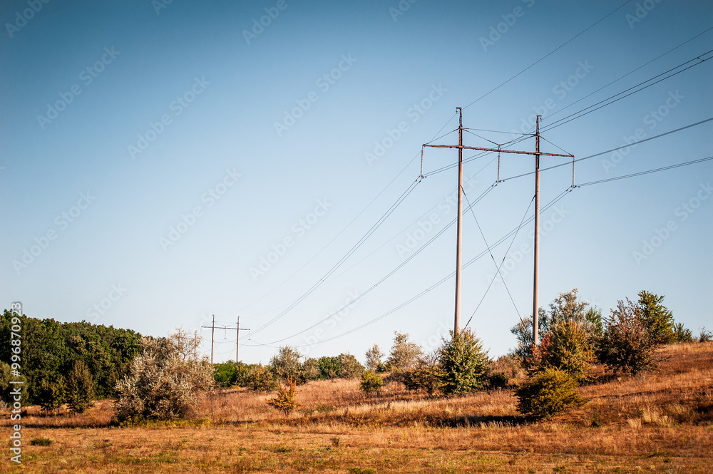 Electric poles connected by wires on hills of dry grass against a blue sky Electric poles connected by wires on hills of dry grass against a blue sky