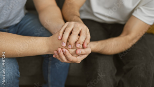 Two men holding hands in a supportive gesture, symbolizing friendship or comfort in a casual indoor setting.