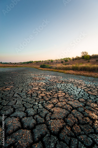Cracks in parched earth, shot at ultra wide angle, revealing yellow hills against a blue sky in the morning
