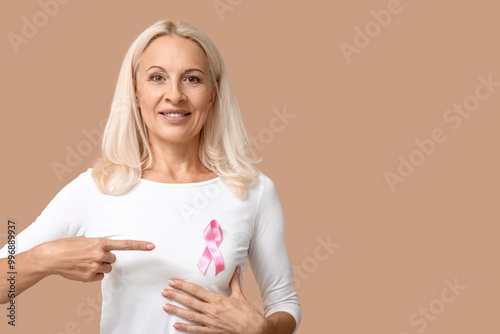 Mature woman with pink ribbon on beige background. Breast cancer awareness concept