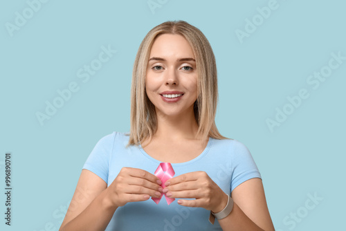 Young woman with pink ribbon on blue background. Breast cancer awareness concept