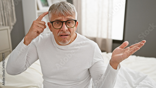 Confused senior man in glasses gesturing in bedroom photo