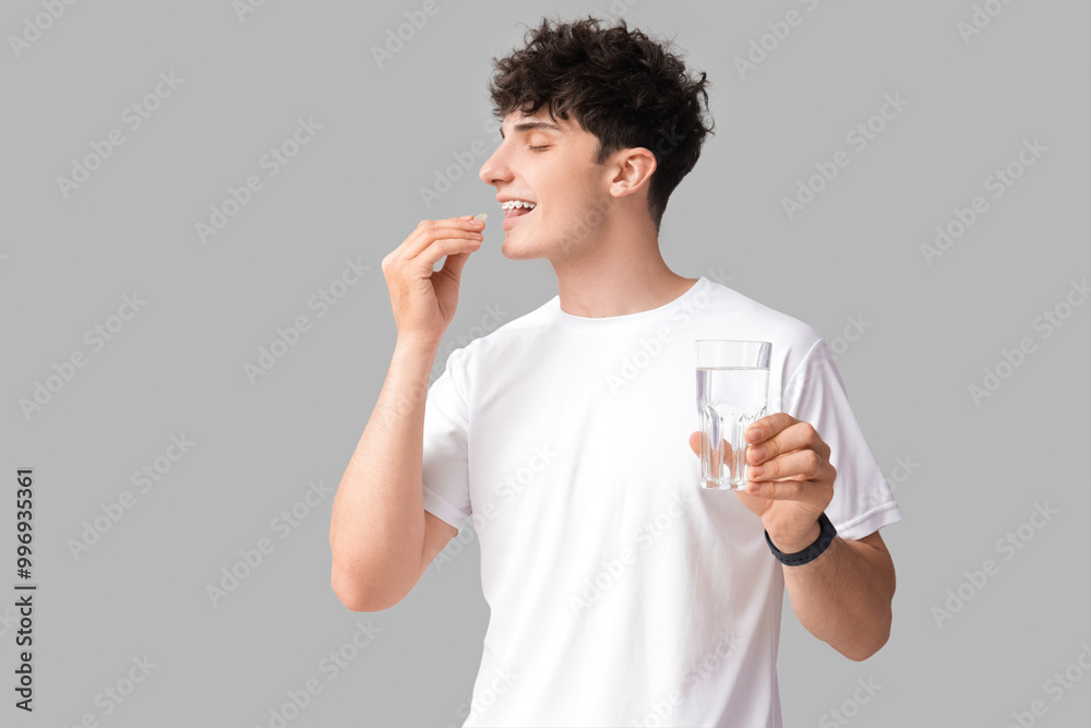 Young man taking fish oil on grey background Young man taking fish oil on grey background
