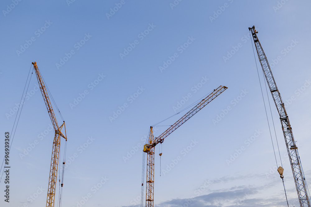 Construction site. Many tower cranes on dusk blue sky background. Construction multi-storey residential and commercial real estate. Industry new building business. Mortgage concept Construction site. Many tower cranes on dusk blue sky background. Construction multi-storey residential and commercial real estate. Industry new building business. Mortgage concept