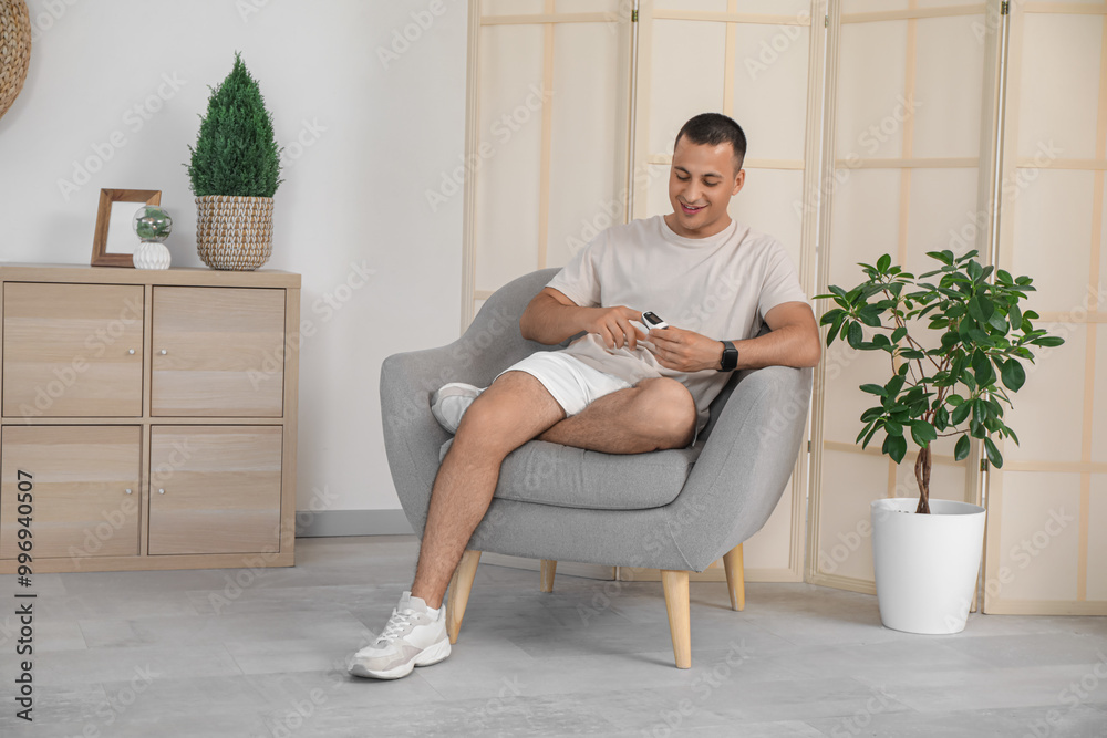 Obraz premium Sporty young man with pulse oximeter sitting in armchair at home
