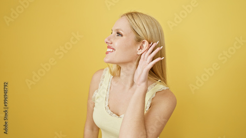 A smiling young blonde woman listens attentively against a vibrant yellow background.