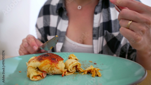 Person in checkered shirt cutting into a serving of homemade enchiladas on a green plate, ready to enjoy a tasty meal photo