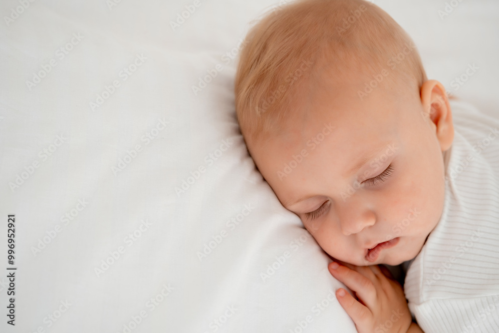 a newborn baby sleeps sweetly on his tummy, a place for text, a baby sleeps on a white bed with a pen under his cheek, a healthy baby's sleep, a close-up portrait a newborn baby sleeps sweetly on his tummy, a place for text, a baby sleeps on a white bed with a pen under his cheek, a healthy baby's sleep, a close-up portrait