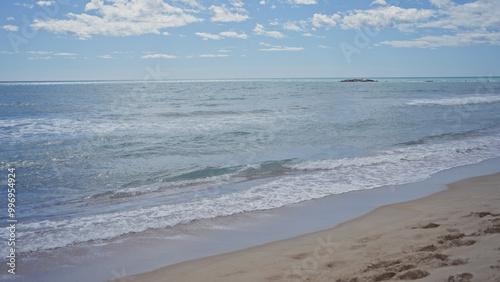 Tranquil beach scene with clear sky, gentle waves, and sandy shore without any people in sight.