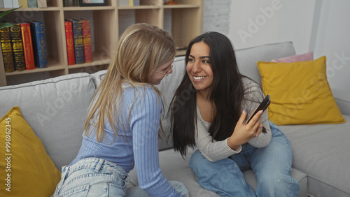 Two women smiling and enjoying time together in a cozy living room, evoking friendship and relaxation. photo