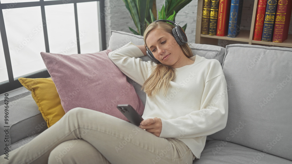 Obraz premium A relaxed young woman enjoying music with headphones and smartphone in a cozy living room on a sofa