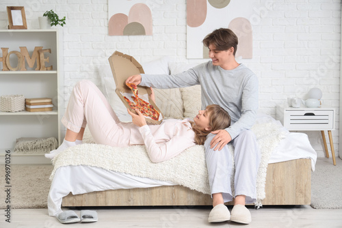 Beautiful young couple with tasty pizza on bed in bedroom