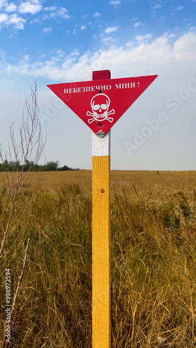 A red warning sign with the inscription Mine Danger and an image of a skull with crossbones on a field background. Mine danger, mine contamination of agricultural fields. Russian-Ukrainian war. Mines