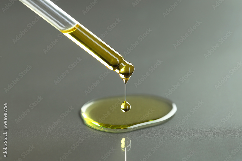 Dripping essential oil from pipette on grey background, closeup Dripping essential oil from pipette on grey background, closeup