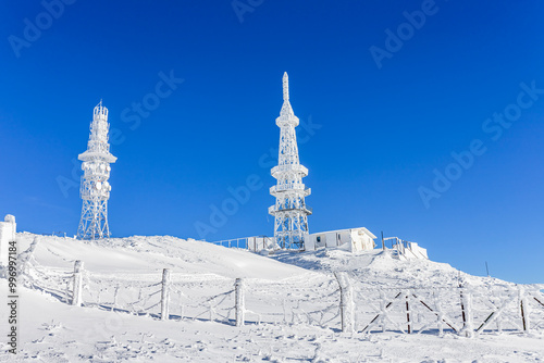 Snow-covered hills and communication towers under a bright blue sky, creating a winter scene.