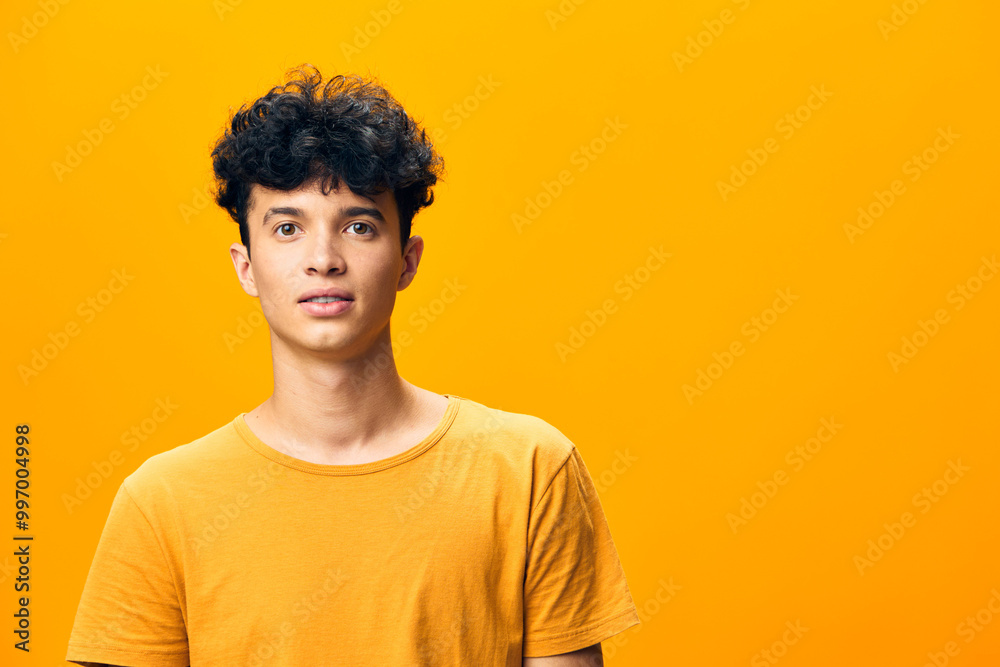 Young man with curly hair in a bright yellow t shirt against a vibrant yellow background, smiling and looking at the camera, conveying happiness and positivity Young man with curly hair in a bright yellow t shirt against a vibrant yellow background, smiling and looking at the camera, conveying happiness and positivity