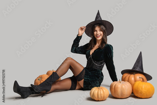 Young witch with Halloween pumpkins on light background photo