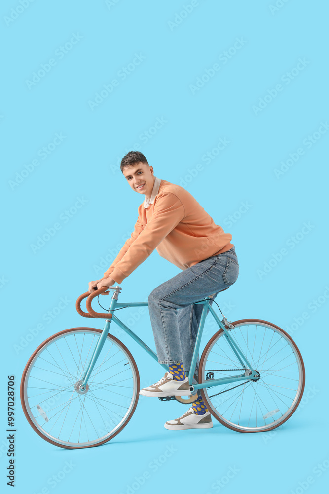 Fototapeta premium Young man in sneakers with bicycle on blue background