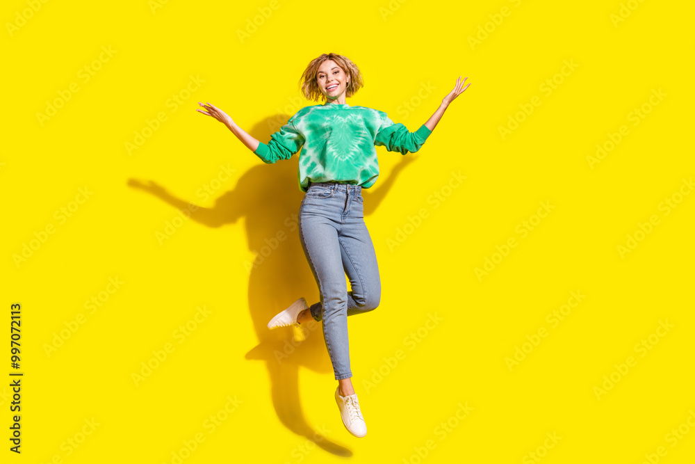 Full length photo of adorable lovely girl wear tie dye sweatshirt jumping high empty space isolated yellow color background Full length photo of adorable lovely girl wear tie dye sweatshirt jumping high empty space isolated yellow color background