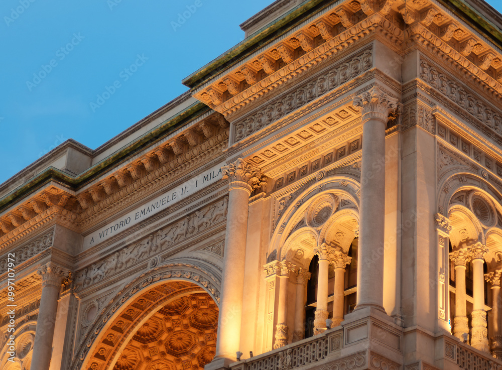 Obraz premium Top of the entrance to the Galleria Vittorio Emanuele II in Milan, with artificial lighting, on a summer evening at the golden hour just before sunset with blue sky