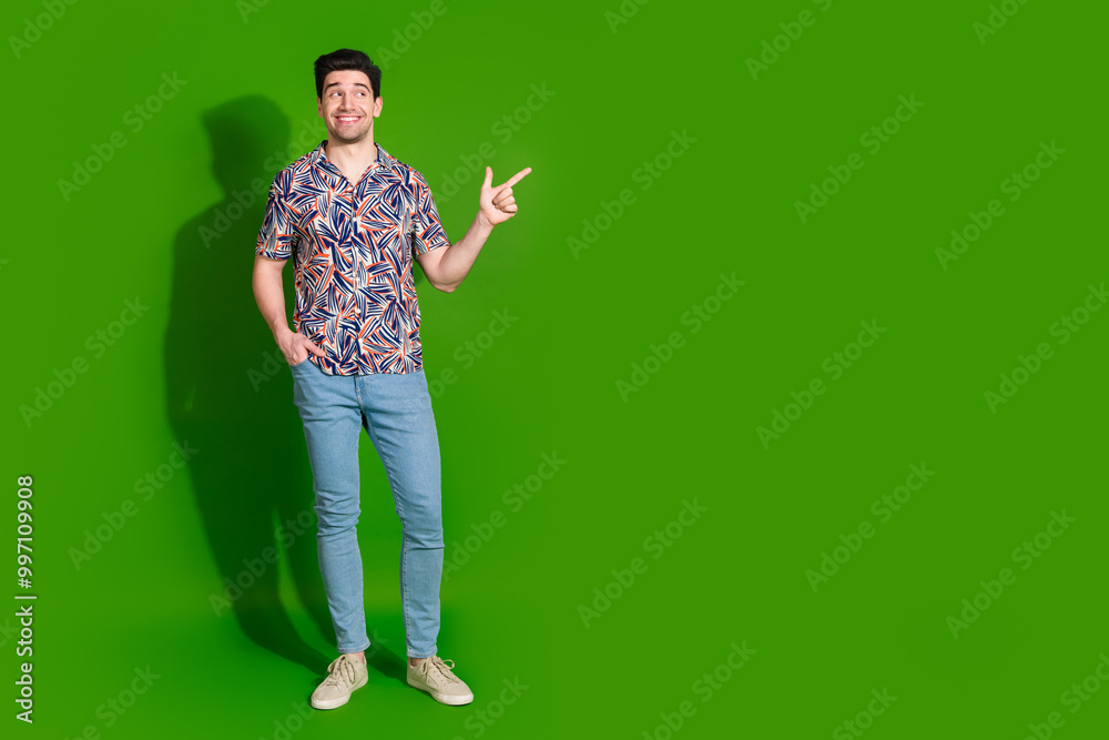 Full length photo of cheerful guy dressed print shirt jeans look directing at offer empty space isolated on green color background Full length photo of cheerful guy dressed print shirt jeans look directing at offer empty space isolated on green color background