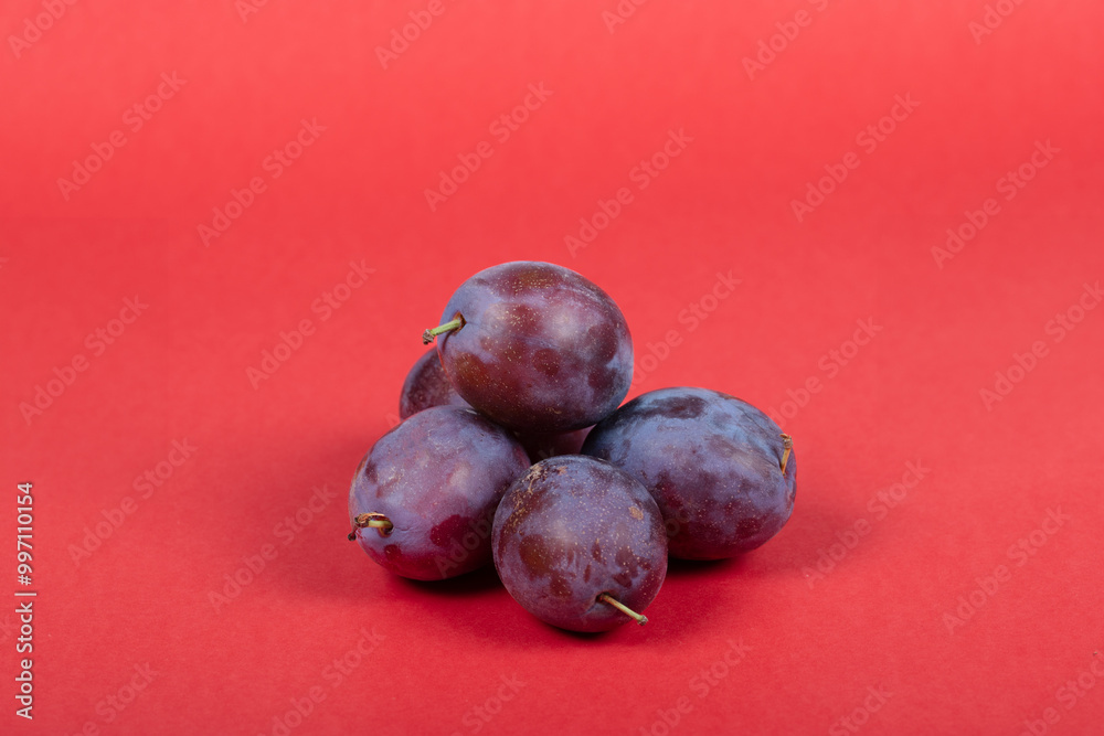 Obraz premium Fresh Purple Plums on Red Background – Isolated Juicy Fruits Perfect for Healthy Eating and Food Photography
