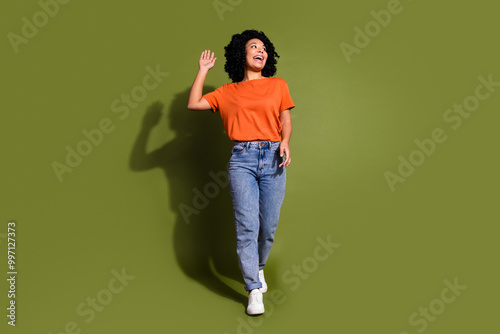 Full length photo of lovely young lady walking wave hand look empty space dressed stylish orange garment isolated on khaki color background