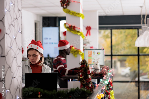 Skillful multiethnical team working in busy xmas adorn modern office during holiday season. Focused coworkers solving business tasks in decorated workplace before Christmas