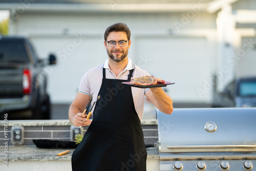 a man in an apron grilling a steak. Barbeque on holiday picnic. Man grilling a steak on BBQ. Grill and barbecue cook. Chef with BBQ cooking tools. Barbecue and grill. Picnic barbecue party.