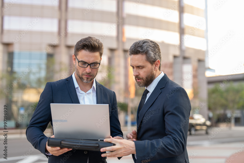 Two entrepreneurs near the office on the street. Business meeting of friends outdoors. Business mens with takeaway coffee and laptop outdoor. Business men team using laptop outdoor. Two businessman Two entrepreneurs near the office on the street. Business meeting of friends outdoors. Business mens with takeaway coffee and laptop outdoor. Business men team using laptop outdoor. Two businessman