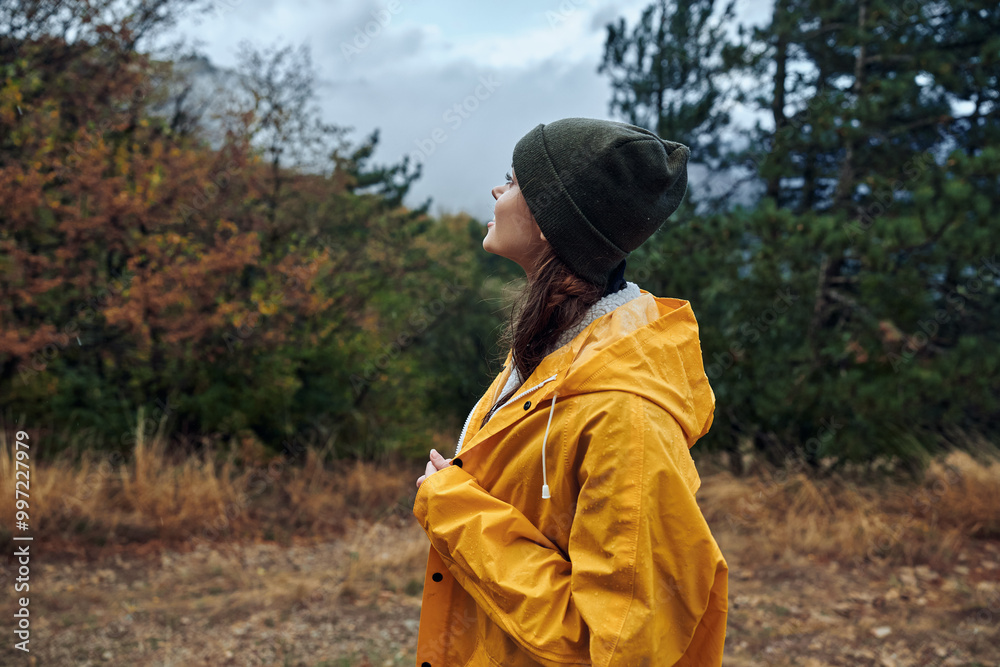 A woman in a yellow raincoat stands in a peaceful field surrounded by trees, showing the beauty of nature with fashion and tranquility