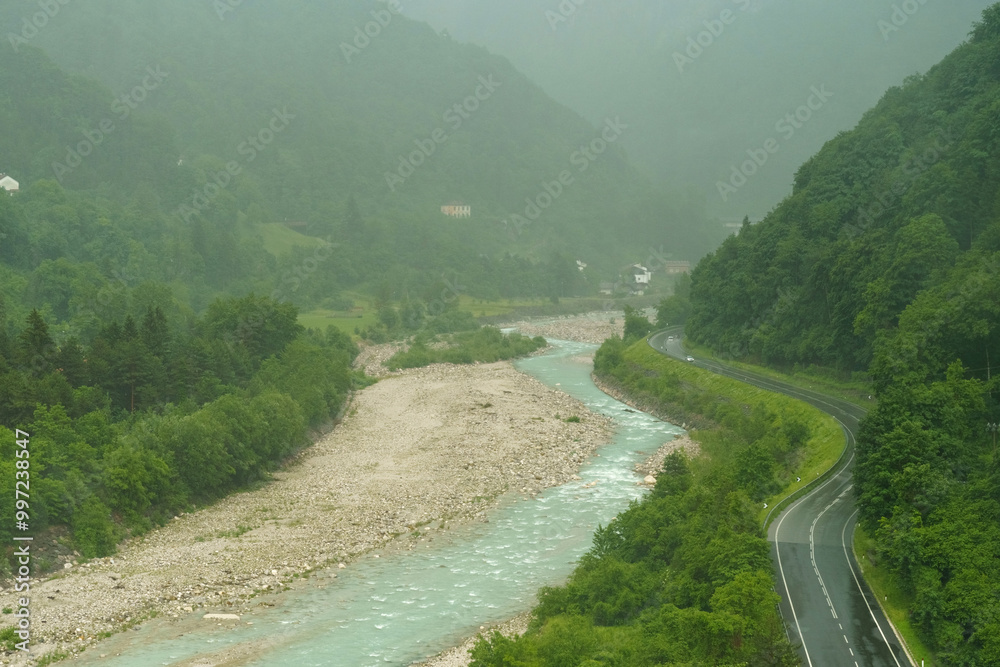 Fototapeta premium A serene river winding through lush green hills on a misty day captures the tranquil beauty of natures landscape