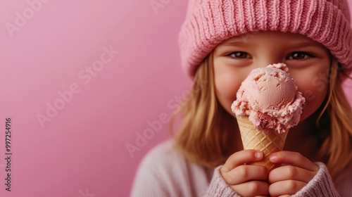 A person in a pink knitted hat and grey sweater holds a small item in their hands against a pink background, portraying a sense of warmth and gentle care.