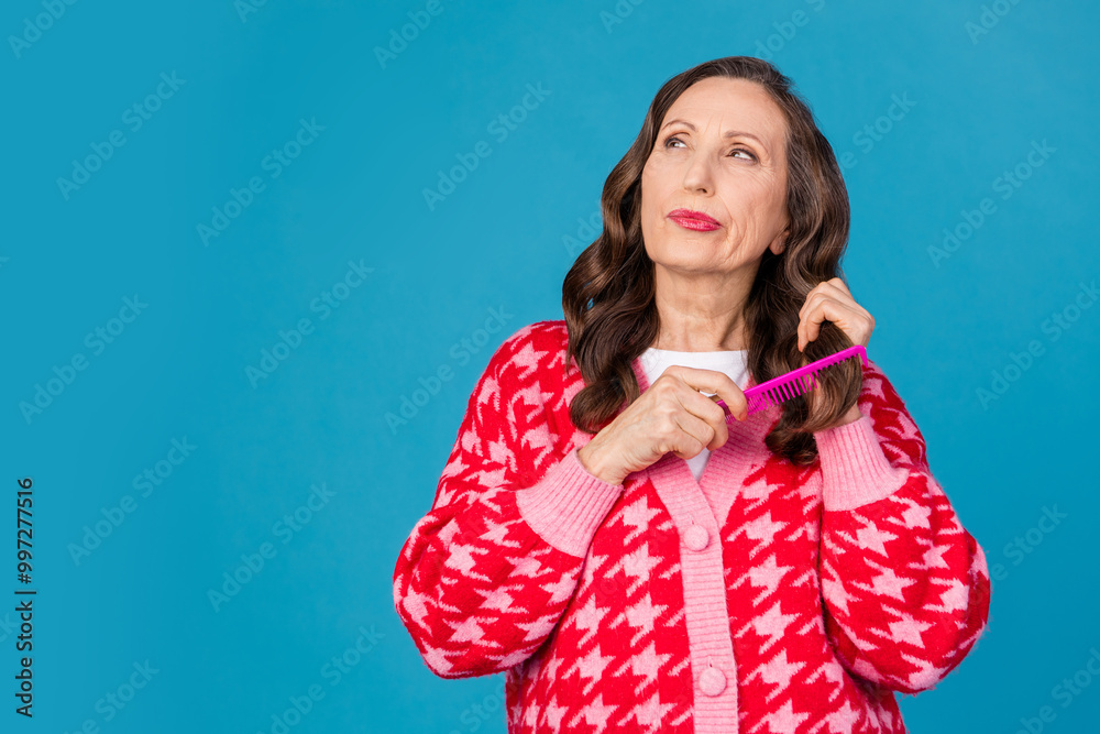 Photo of lovely senior lady touch brush hair look unsure empty space dressed stylish pink print garment isolated on blue color background Photo of lovely senior lady touch brush hair look unsure empty space dressed stylish pink print garment isolated on blue color background