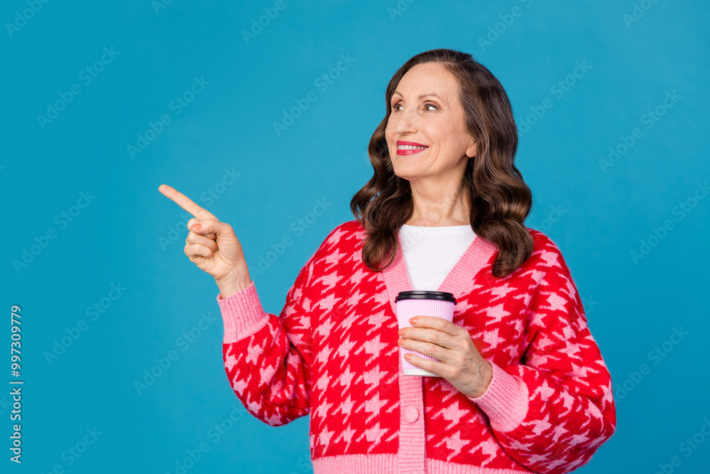 Photo of nice pensioner female look point empty space hold coffee paper cup wear trendy pink print outfit isolated on blue color background Photo of nice pensioner female look point empty space hold coffee paper cup wear trendy pink print outfit isolated on blue color background