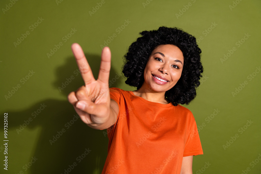 Photo portrait of lovely young lady show v-sign cheerful smile dressed stylish orange garment isolated on khaki color background Photo portrait of lovely young lady show v-sign cheerful smile dressed stylish orange garment isolated on khaki color background
