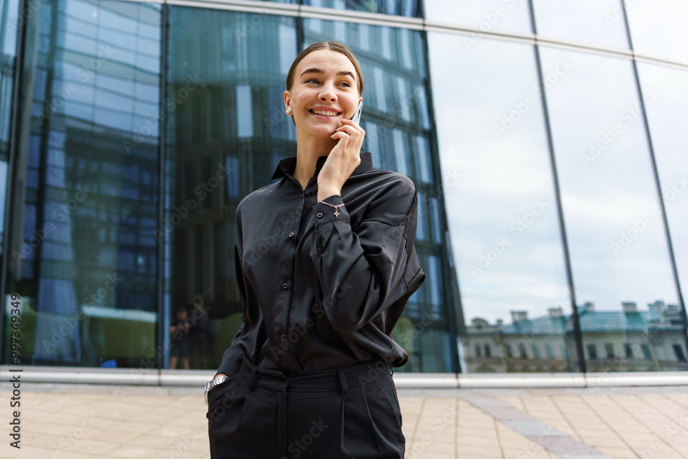 Professional Woman Talking on Mobile Phone Near Modern Glass Building in a City on a Cloudy Day Professional Woman Talking on Mobile Phone Near Modern Glass Building in a City on a Cloudy Day