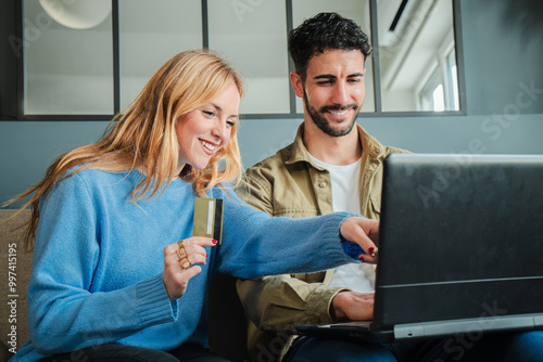 Tablou pe pânză Couple using a laptop to make an online purchase with a credit card, smiling whi