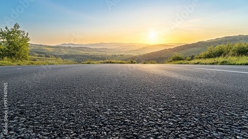 A smooth asphalt road stretches into the horizon, illuminated by the soft golden light of the rising sun, surrounded by lush green hills and valleys