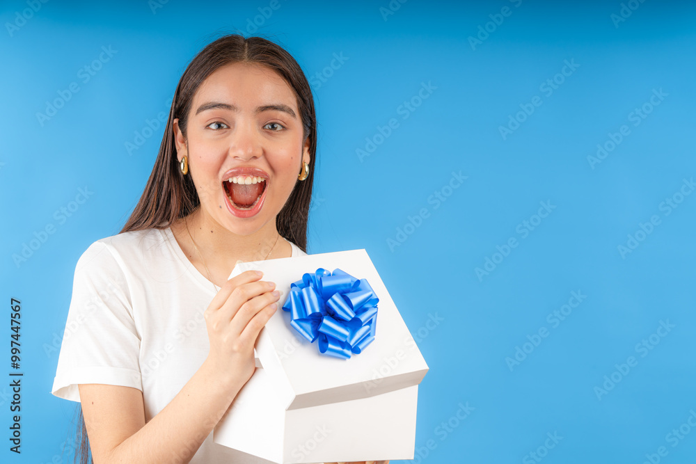 Excited woman holding a gift with blue ribbon on blue background Excited woman holding a gift with blue ribbon on blue background