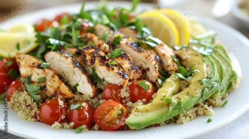 A healthy and colorful quinoa salad with grilled chicken, avocado, cherry tomatoes, and a light lemon dressing, served on a white plate